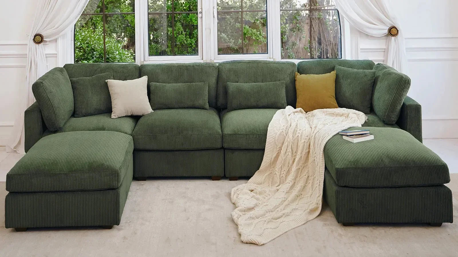 Dark‑green corduroy modular L‑shaped sectional sofa with throw pillows and knitted blanket