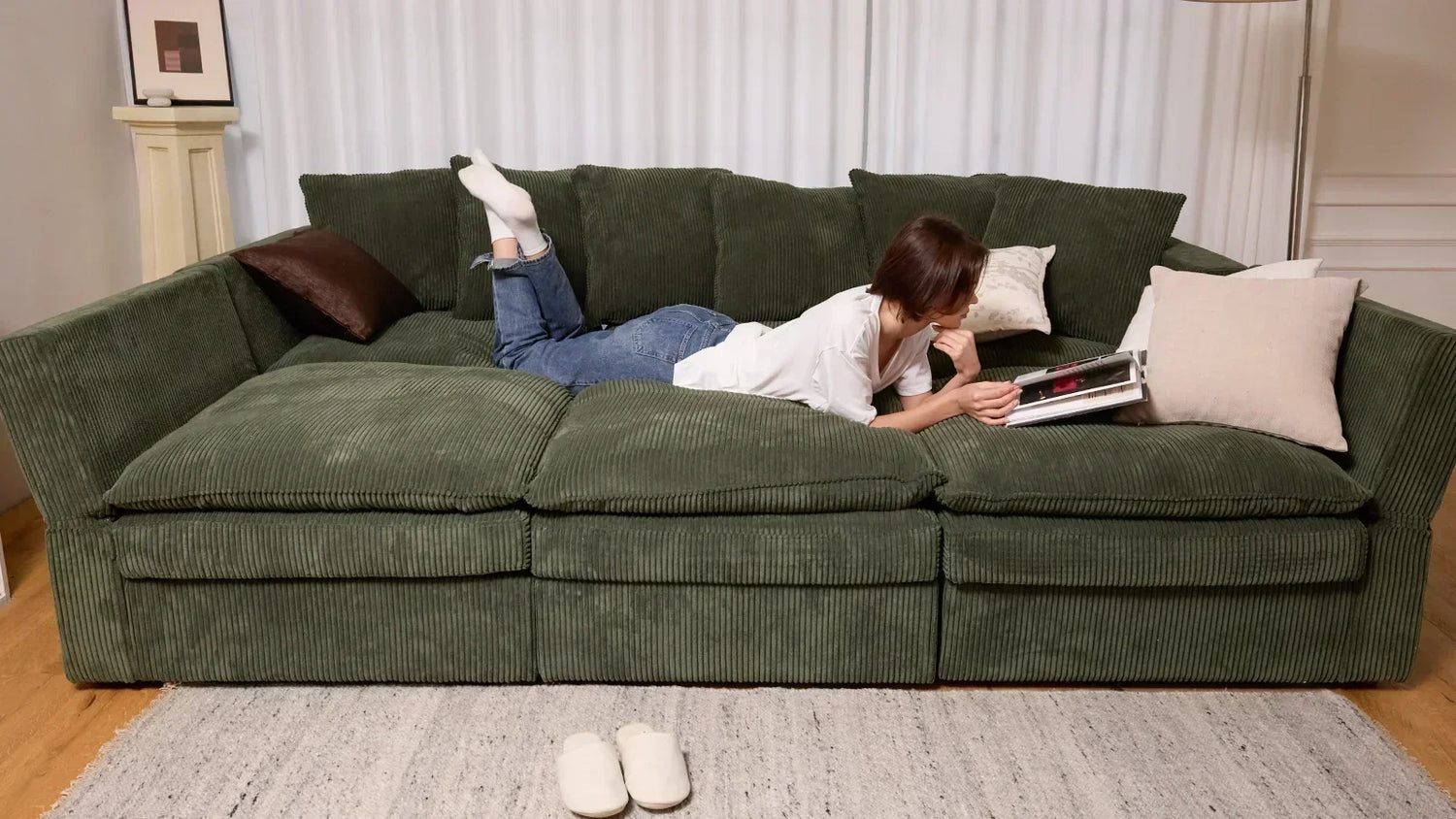 Woman relaxing on a green corduroy modular sleeper sectional with storage in a bright living room