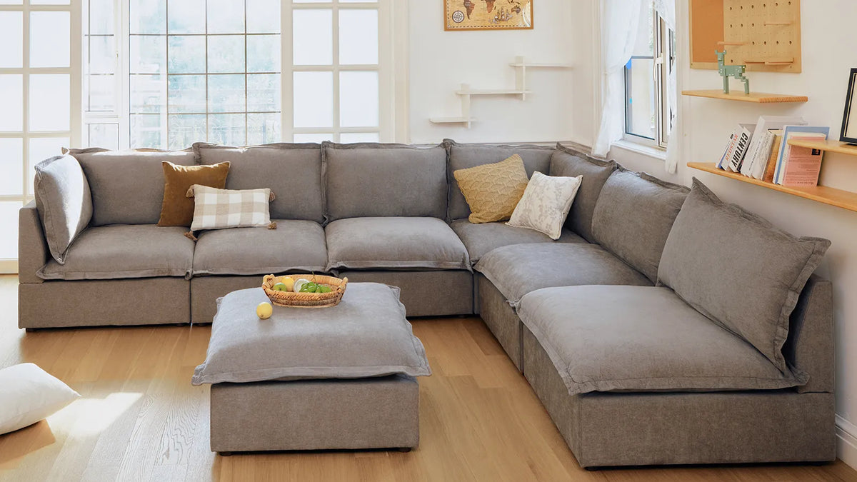 Gray L-shaped modular sectional sofa in a bright living room with ottoman